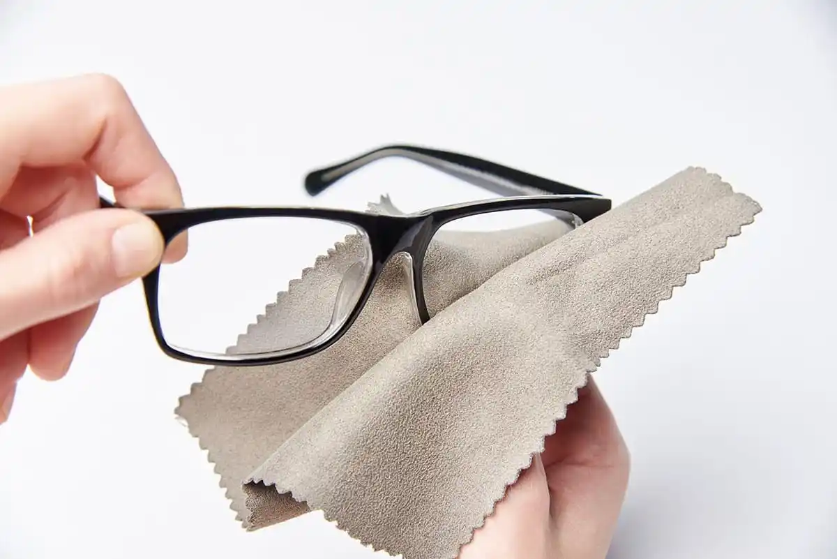Eine Brille wird mit einem Reinigungstuch sorgfältig von einer Hand geputzt