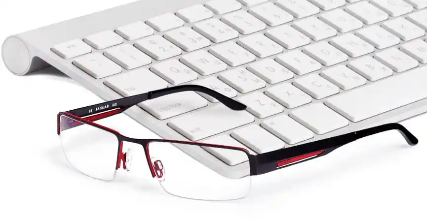 Brille mit schwarzem und rotem Gestell auf einer Tastatur, als Nahaufnahme dargestellt.