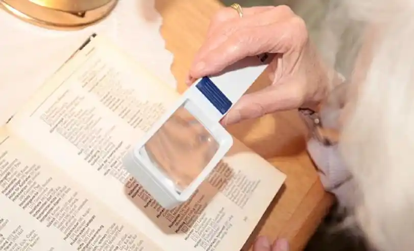 Frau betrachtet einen Text aus der Nähe und nutzt eine Lupe zum Vergrößern der Schrift.