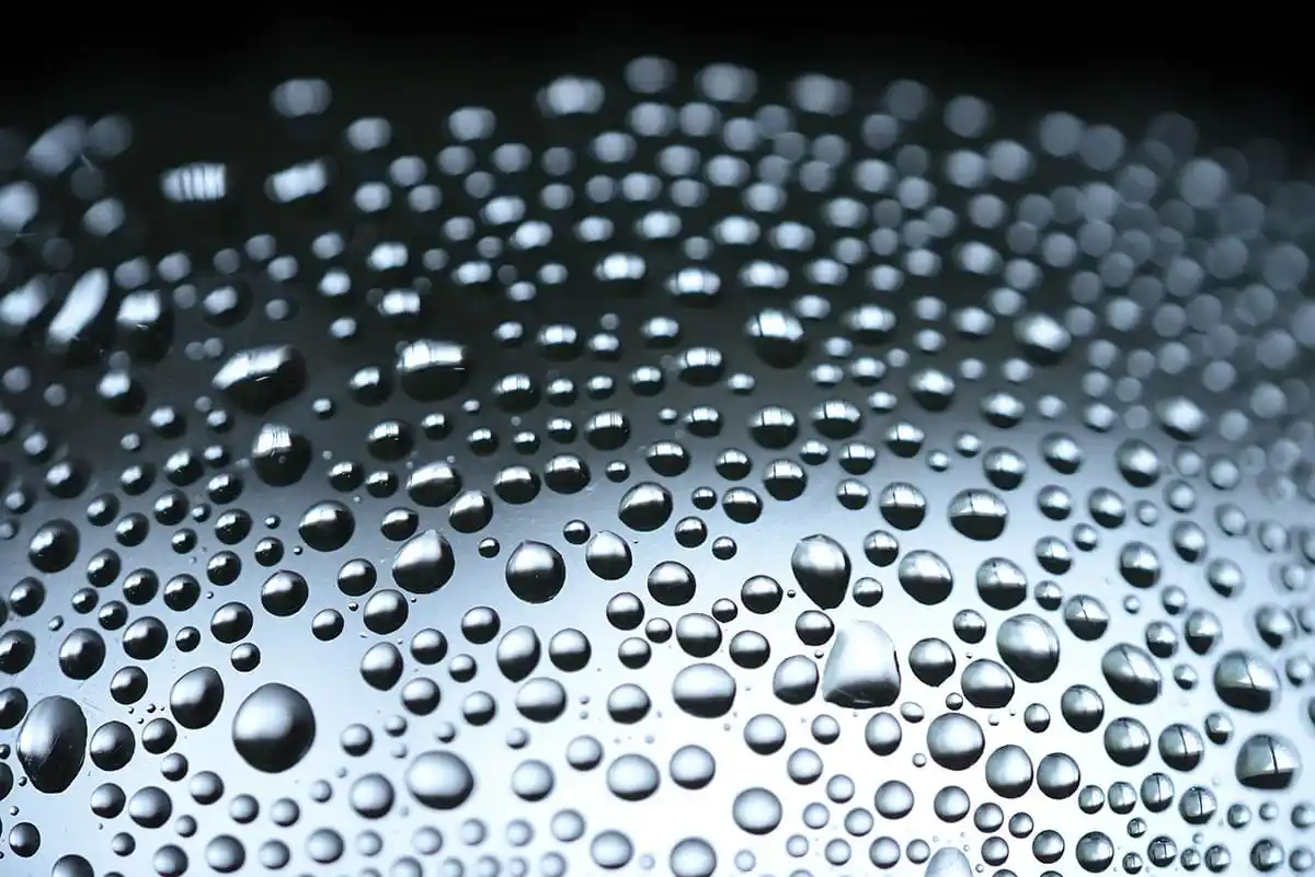 Tropfen Flüssigkeit in Close-up, mit sichtbarer Oberflächenspannung und Lichtreflexionen