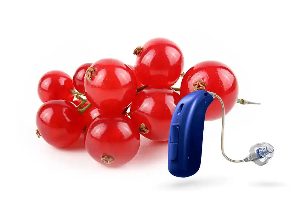 Kleines Hörgerät im Vergleich zu roten Johannisbeeren als Größenvergleich arrangiert.