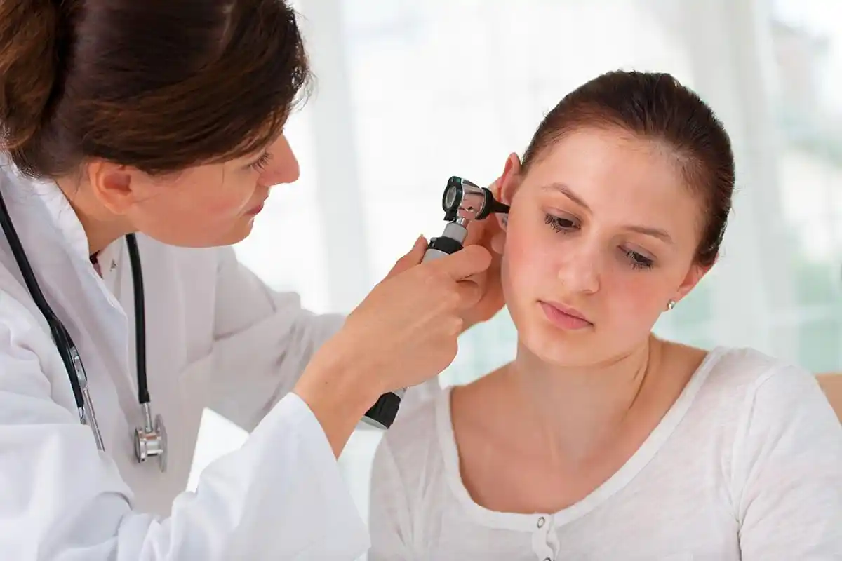 Ein Arzt untersucht das Ohr einer Patientin mit einem Otoskop in einer medizinischen Untersuchungssituation