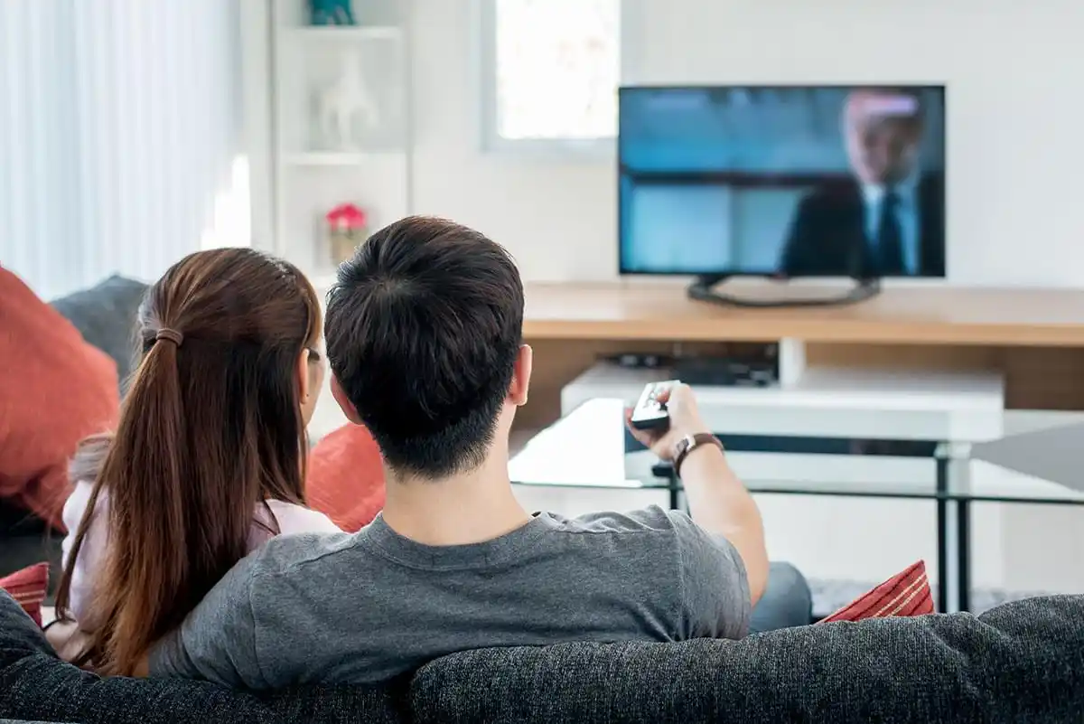 Ein Paar sitzt gemeinsam auf einem Sofa und schaut entspannt fernsehen im Wohnzimmer
